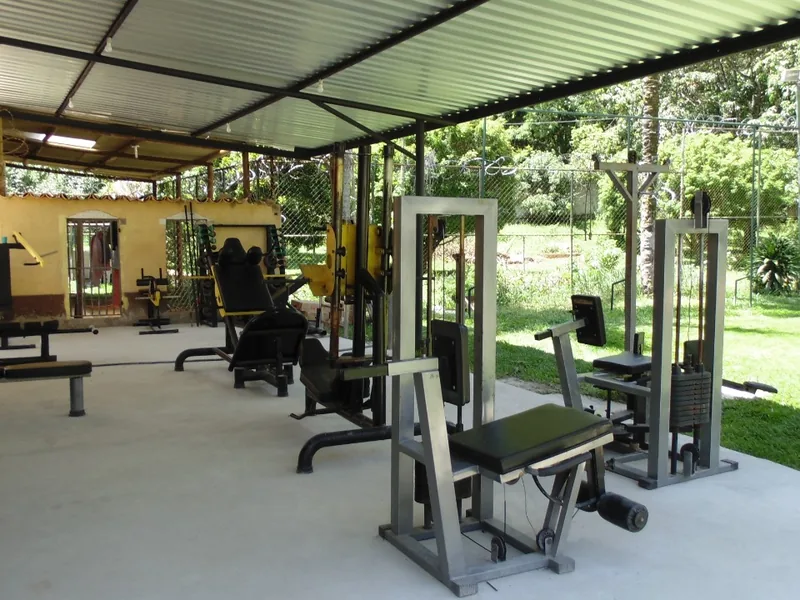 Sala com aparelhos de musculação sob cobertura, aberta para o verde